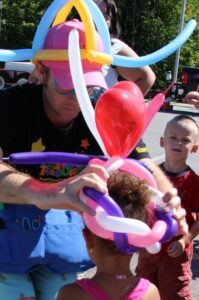 balloon man giving young girl a balloon hat at 2nd annual community celebration