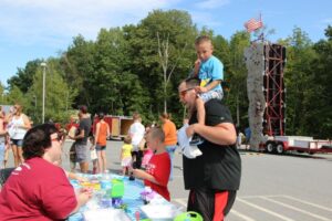 man and two boys talking to woman volunteer at table at 2nd annual community celebration