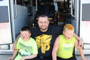 man with two boys in back of ambulance at 2nd annual community celebration