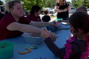 woman handing out cereal necklace to young girl at 3rd annual community celebration