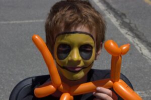 young boy in face paint with balloon animal at 3rd annual community celebration