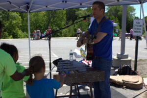 man with guitar and girls playing xylophone at 3rd annual community celebration