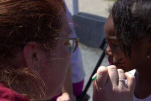 woman giving cat face paint to young girl at 3rd annual community celebration